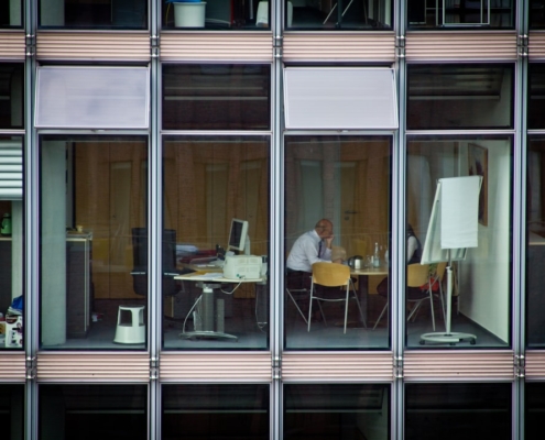 Un dirigeant senior seul ou en petit comité, dans un environnement de bureau moderne et sobre, en posture de réflexion ou d'analyse — lumière naturelle froide, palette neutre anthracite/blanc/gris, atmosphère de concentration stratégique sans action caricaturale.