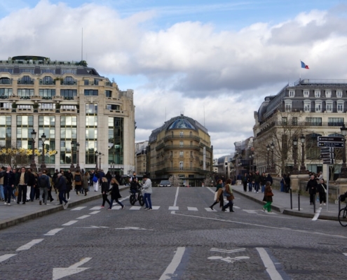 Image grand format sobre et premium. Scène de négociation ou de signature d'accord entre dirigeants dans un cadre business parisien reconnaissable — La Défense en arrière-plan ou vitres d'un cabinet haut de gamme. Tonalité froide et professionnelle : gris acier, bleu nuit, lumière naturelle tamisée. Aucun billet, aucune poignée de main cliché. Préférer un plan large ou demi-ensemble montrant deux interlocuteurs face à des documents contractuels, contexte international lisible (documents multilingues, carte du monde, drapeaux discrets).